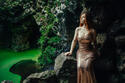 Young woman wearing gold dress sitting on rocks by green river