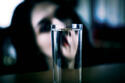 Young woman with distorted face behind glass of water